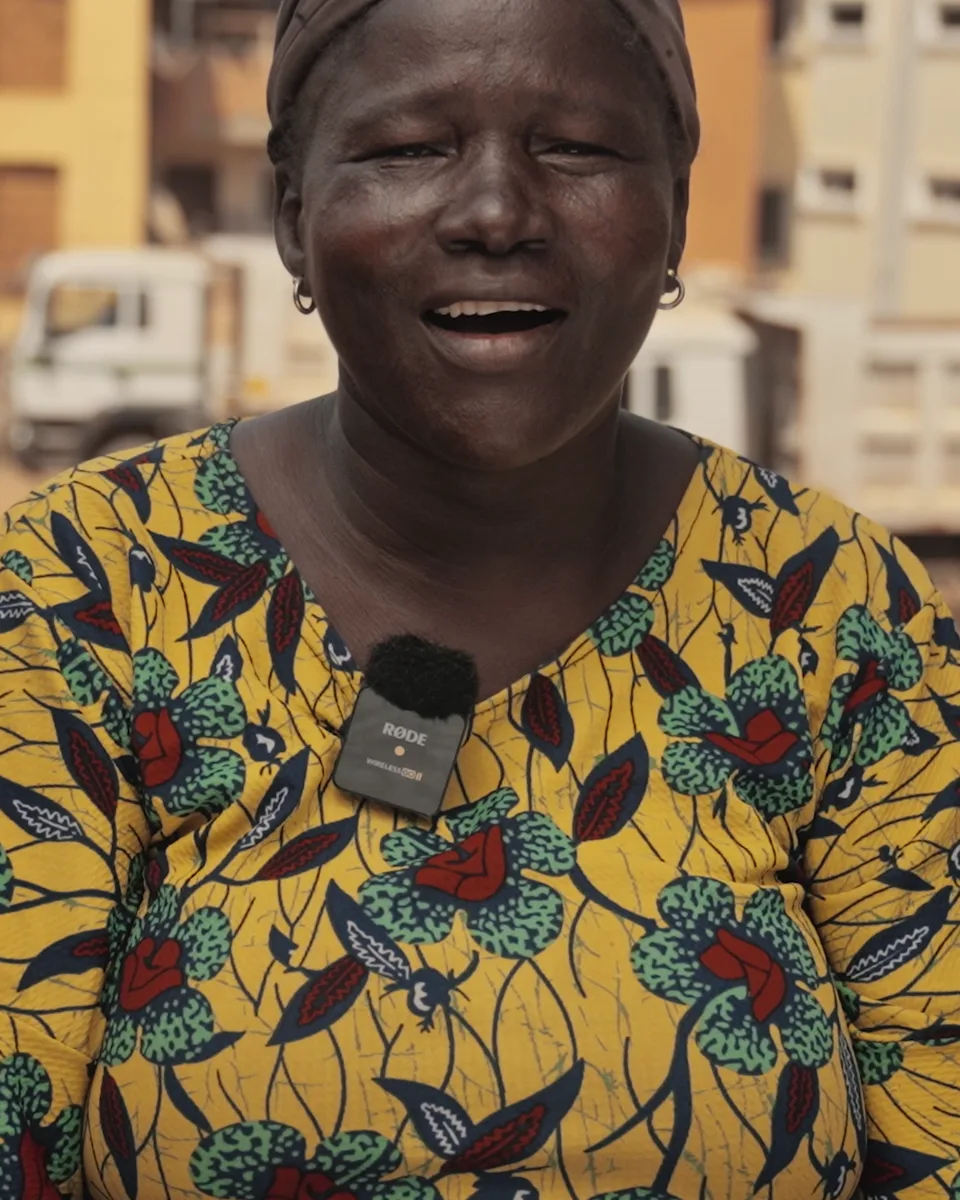 Three women of Mabushi, Abuja, singing, with a truck and cleared ground behind them