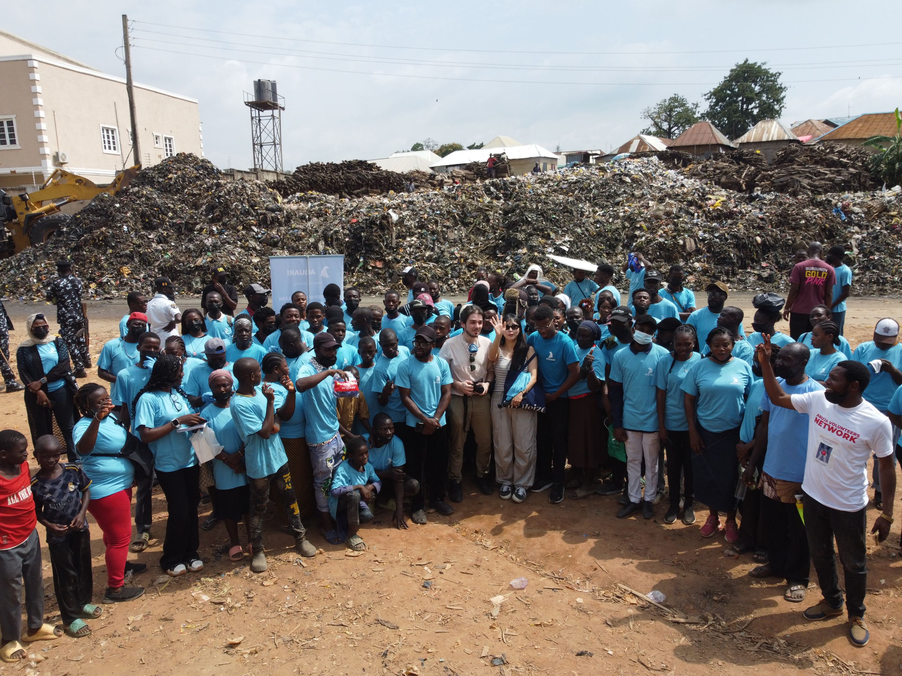 More than a hundred people, most in light blue shirts, standing together in front of the waste pile